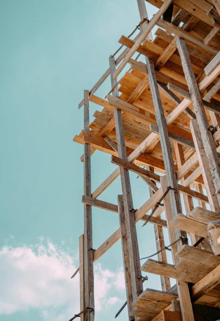Wooden scaffolding structure against a blue sky with some clouds, viewed from below.
